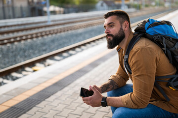 Adult man is sitting at railway station and waiting for arrival of train.
