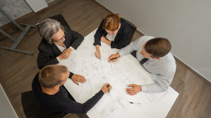 Top view of 4 business people sitting at a table and discussing blueprints. Designers engineers at...