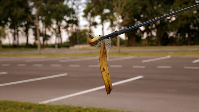 A close-up of an activist collecting garbage with tongs in an urban area, plastic garbage and a banana skin. 