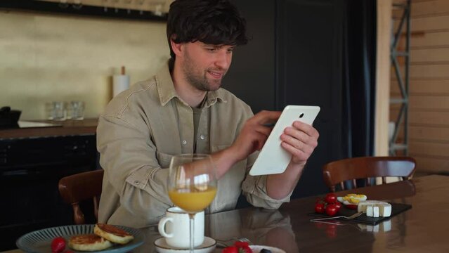 Man works on a tablet, uses free Internet access, drinks orange juice and eats a delicious breakfast. 