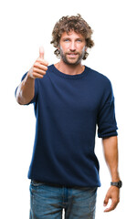 Handsome hispanic model man wearing winter sweater over isolated background doing happy thumbs up gesture with hand. Approving expression looking at the camera with showing success.