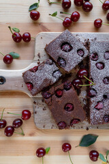 Chocolate cake with sour cherries on light wooden table