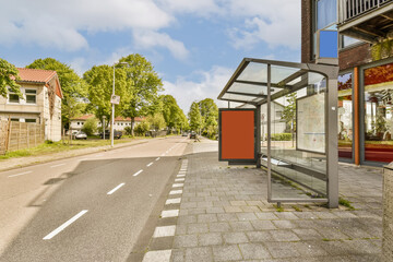 a bus stop in the middle of an empty street with buildings and trees on both sides, as seen from the side