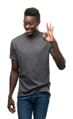 Young african american man wearing grey t-shirt smiling positive doing ok sign with hand and fingers. Successful expression.