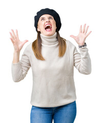 Middle age mature woman wearing winter sweater and beret over isolated background crazy and mad shouting and yelling with aggressive expression and arms raised. Frustration concept.