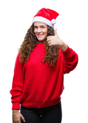 Young brunette girl wearing christmas hat over isolated background doing happy thumbs up gesture with hand. Approving expression looking at the camera with showing success.