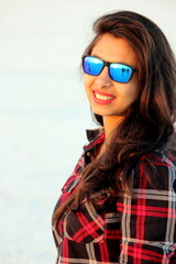 A woman wearing checks shirt and a sunglass. Bright smiling face of a girl suitable for travel, holidays,  adventure, vacation business. Portrait photo of a model with white background