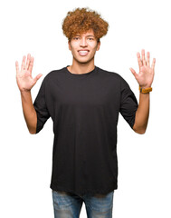 Young handsome man with afro hair wearing black t-shirt showing and pointing up with fingers number ten while smiling confident and happy.