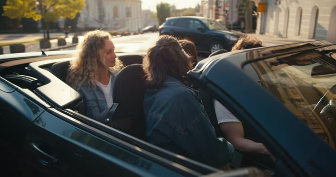 Happy friends in a dark gray convertible have arrived at their destination and are parking their car, they are chatting and having fun