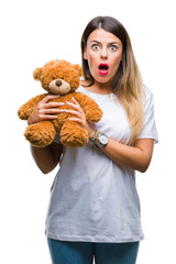 Young beautiful woman holding teddy bear plush over isolated background scared in shock with a surprise face, afraid and excited with fear expression