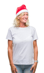 Middle age blonde woman wearing christmas hat over isolated background looking away to side with smile on face, natural expression. Laughing confident.