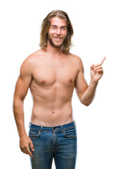 Young handsome shirtless man with long hair showing sexy body over isolated background with a big smile on face, pointing with hand and finger to the side looking at the camera.