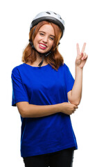 Young beautiful woman wearing cyclist helmet over isolated background smiling with happy face winking at the camera doing victory sign. Number two.