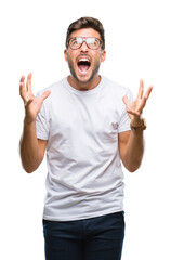 Fototapeta premium Young handsome man wearing glasses over isolated background crazy and mad shouting and yelling with aggressive expression and arms raised. Frustration concept.
