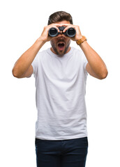 Young handsome man looking through binoculars over isolated background scared in shock with a...