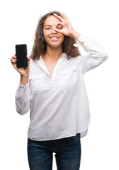 Fototapeta premium Young hispanic woman using smartphone with happy face smiling doing ok sign with hand on eye looking through fingers
