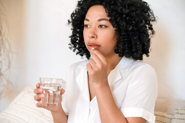 african american woman hold glas of water and taking medication