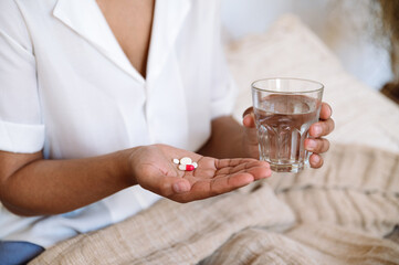 female hands hold glass of water and painkiller pills