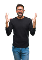 Adult hispanic man wearing glasses over isolated background celebrating mad and crazy for success with arms raised and closed eyes screaming excited. Winner concept