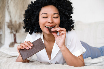Fototapeta na wymiar happy woman eating chocolate while lying in bed