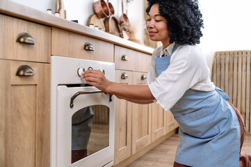 afro american housewife turn on electric oven to cooking dinner