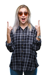 Young blonde woman wearing sunglasses over isolated background amazed and surprised looking up and pointing with fingers and raised arms.