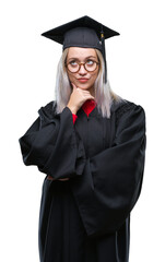 Young blonde woman wearing graduate uniform over isolated background with hand on chin thinking about question, pensive expression. Smiling with thoughtful face. Doubt concept.