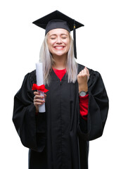 Young blonde woman wearing graduate uniform holding degree over isolated background screaming proud...