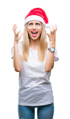 Fototapeta na wymiar Young beautiful blonde woman christmas hat over isolated background crazy and mad shouting and yelling with aggressive expression and arms raised. Frustration concept.