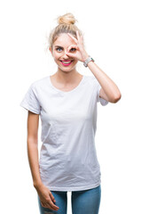 Young beautiful blonde woman wearing white t-shirt over isolated background doing ok gesture with hand smiling, eye looking through fingers with happy face.