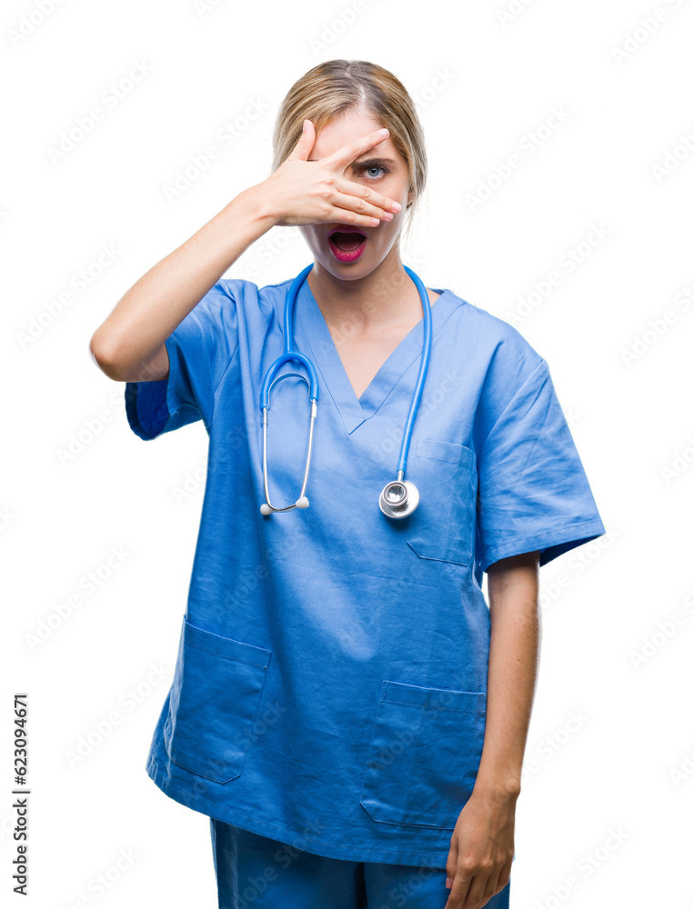 Poster Young beautiful blonde doctor surgeon nurse woman over isolated background peeking in shock covering face and eyes with hand, looking through fingers with embarrassed expression.