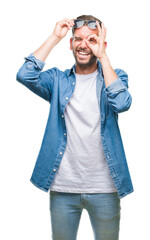 Fototapeta premium Young handsome man wearing sunglasses over isolated background doing ok gesture with hand smiling, eye looking through fingers with happy face.