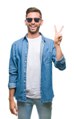 Young handsome man wearing sunglasses over isolated background smiling with happy face winking at the camera doing victory sign. Number two.