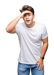 Young handsome man wearing white t-shirt over isolated background very happy and smiling looking far away with hand over head. Searching concept.