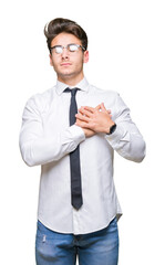 Young business man wearing glasses over isolated background smiling with hands on chest with closed eyes and grateful gesture on face. Health concept.