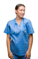Young caucasian doctor woman wearing medical uniform over isolated background looking away to side with smile on face, natural expression. Laughing confident.