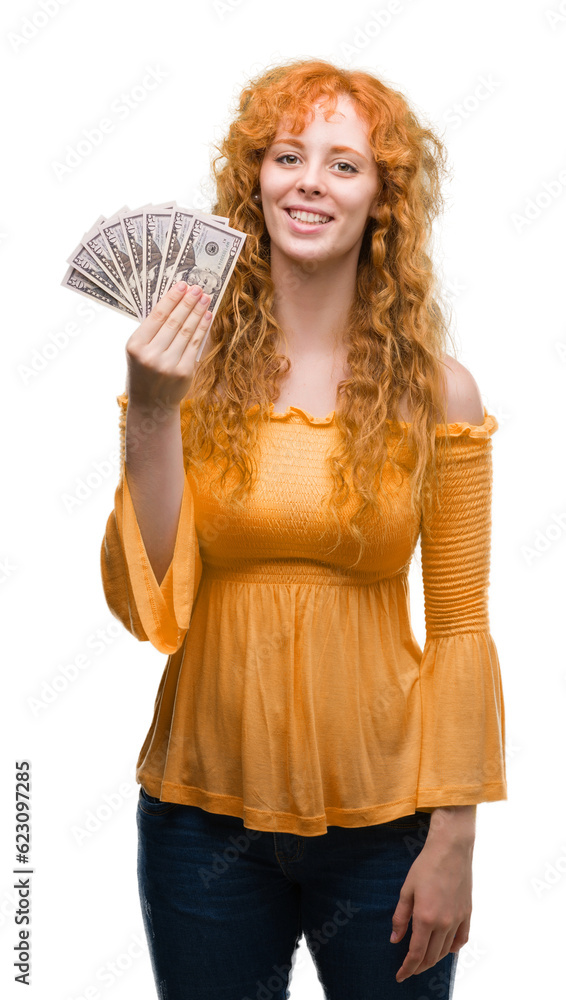 Wall mural young redhead woman holding dollars with a happy face standing and smiling with a confident smile sh