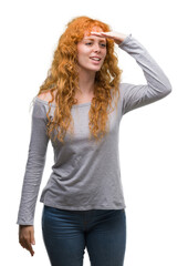 Young redhead woman very happy and smiling looking far away with hand over head. Searching concept.