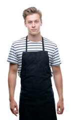 Young handsome blond man wearing apron with a confident expression on smart face thinking serious