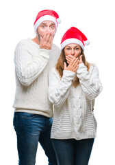 Middle age hispanic couple wearing christmas hat over isolated background shocked covering mouth with hands for mistake. Secret concept.