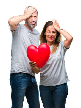 Middle age hispanic casual couple in love holding red heart over isolated background stressed with hand on head, shocked with shame and surprise face, angry and frustrated. Fear and upset for mistake.