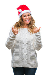 Middle age senior hispanic woman wearing christmas hat over isolated background success sign doing positive gesture with hand, thumbs up smiling and happy. Looking at the camera