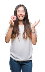 Obraz na płótnie Canvas Young asian woman eating donut over isolated background very happy and excited, winner expression celebrating victory screaming with big smile and raised hands