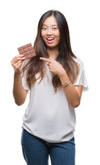 Young asian woman eating chocolate bar over isolated background very happy pointing with hand and finger