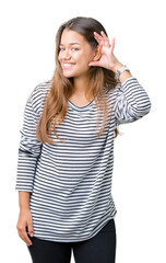 Obraz na płótnie Canvas Young beautiful brunette woman wearing stripes sweater over isolated background smiling with hand over ear listening an hearing to rumor or gossip. Deafness concept.