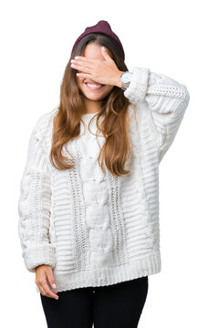 Young beautiful brunette hipster woman wearing glasses and winter hat over isolated background smiling and laughing with hand on face covering eyes for surprise. Blind concept.