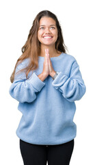 Young beautiful brunette woman wearing blue winter sweater over isolated background praying with hands together asking for forgiveness smiling confident.