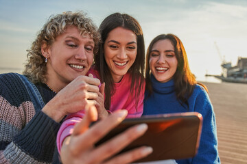 Waist up of smiling attractive girls sitting with man friend in pier and taking photo