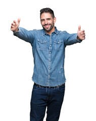 Fototapeta premium Young handsome man over isolated background looking at the camera smiling with open arms for hug. Cheerful expression embracing happiness.