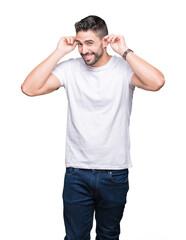Fototapeta premium Young man wearing casual white t-shirt over isolated background covering ears with fingers with annoyed expression for the noise of loud music. Deaf concept.